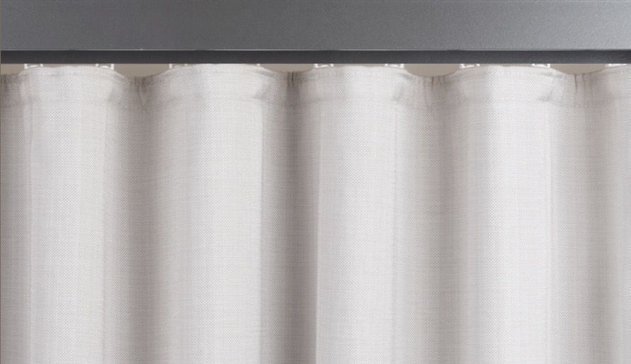 Off-white, textured curtains hanging from a gray track, creating vertical folds.