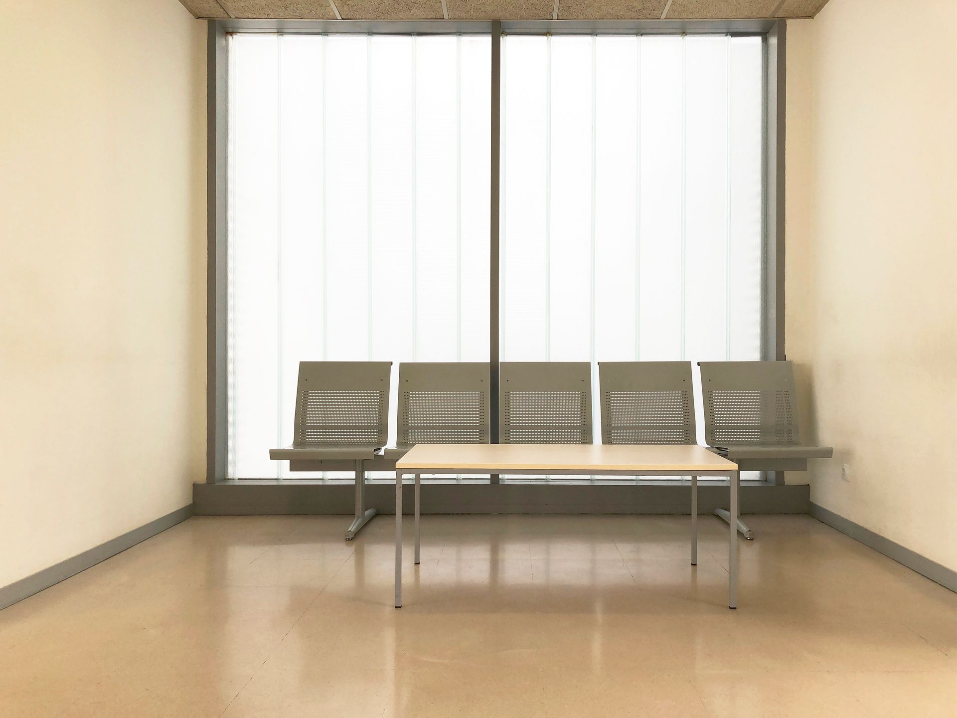 An empty waiting room with chairs and a table in front of a large window.
