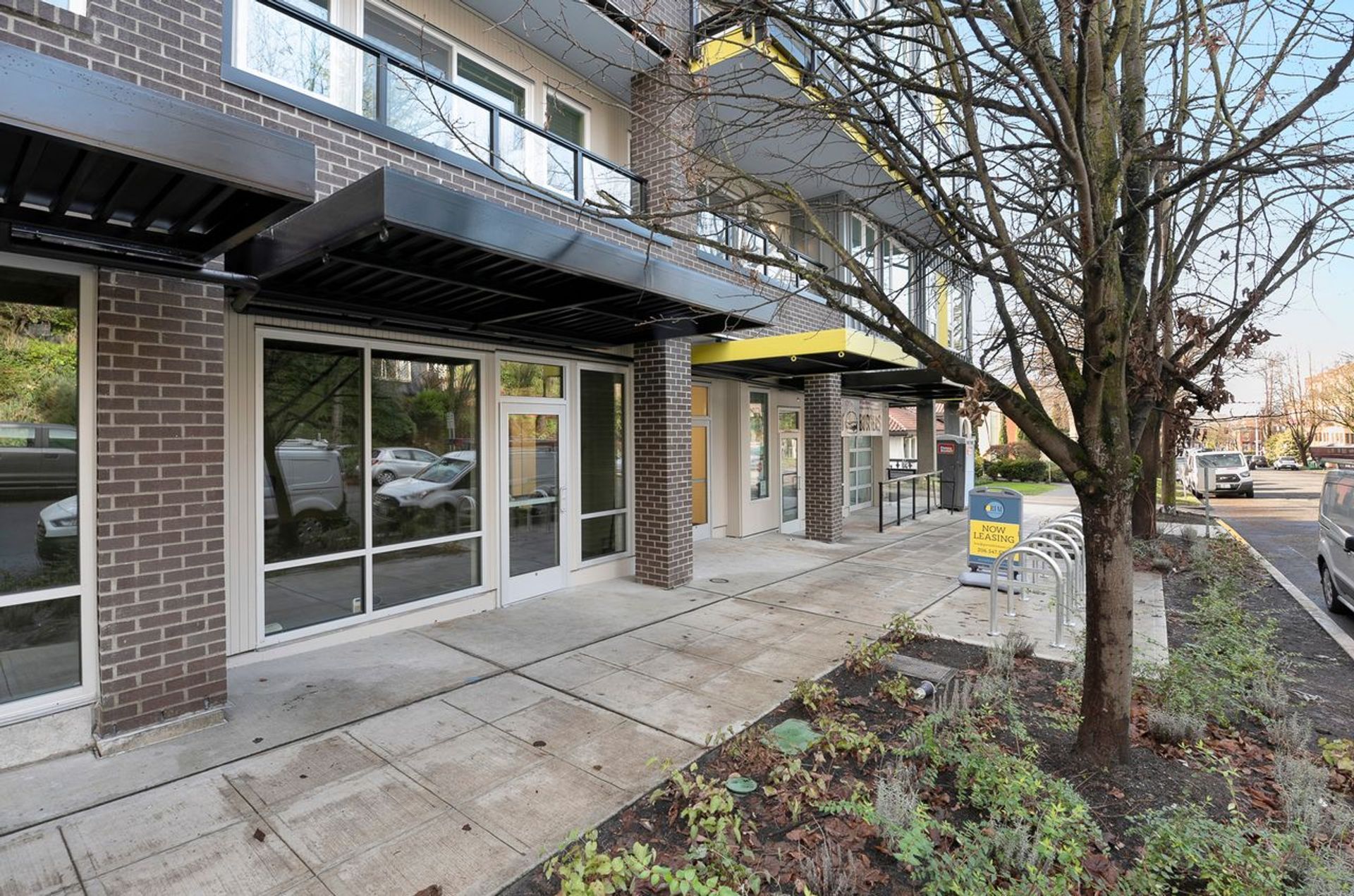 Photo of the entrance to the building, seen from the sidewalk, with a bike rack and plants outside