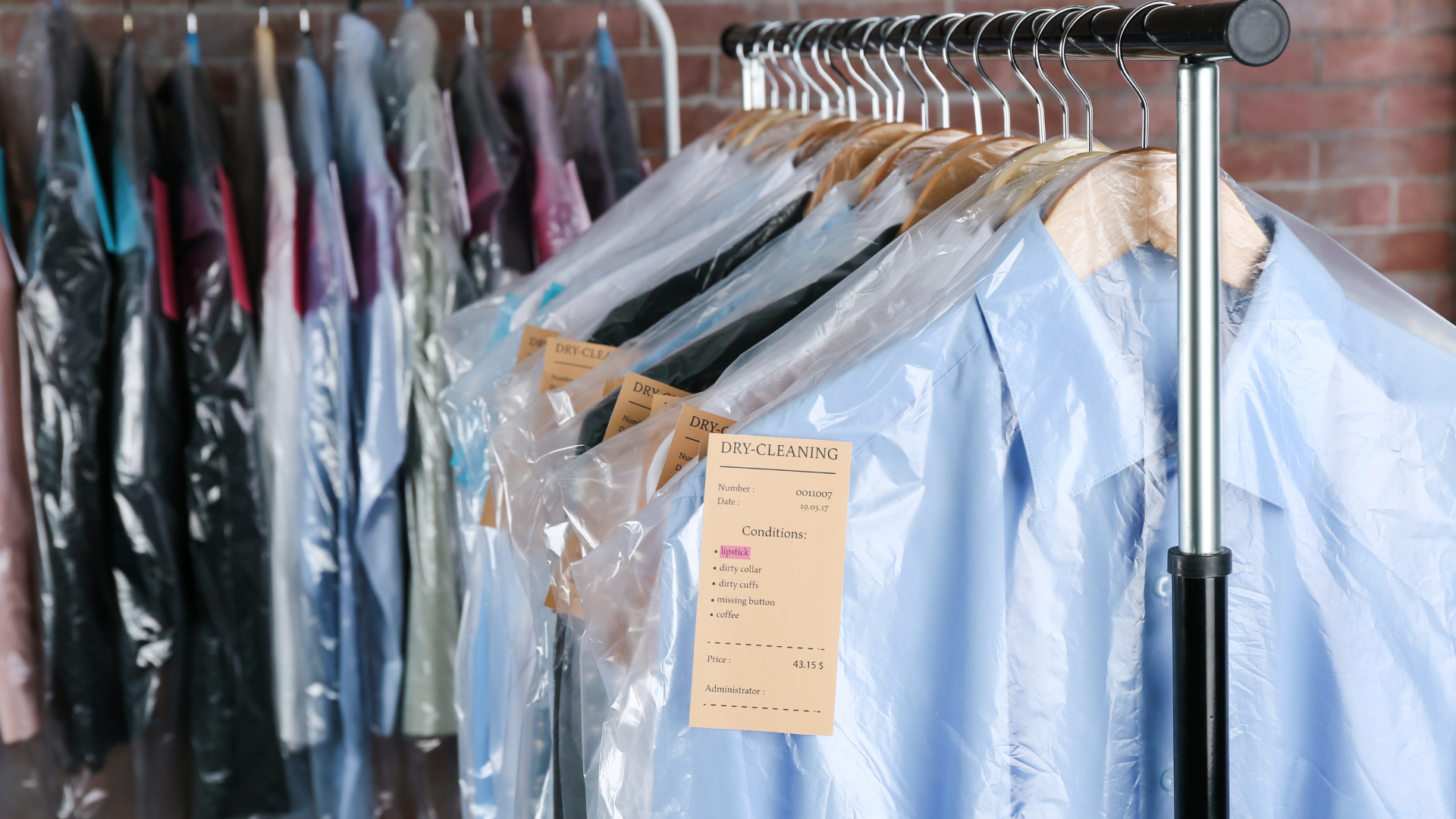 A row of shirts hanging on a rack in plastic bags.
