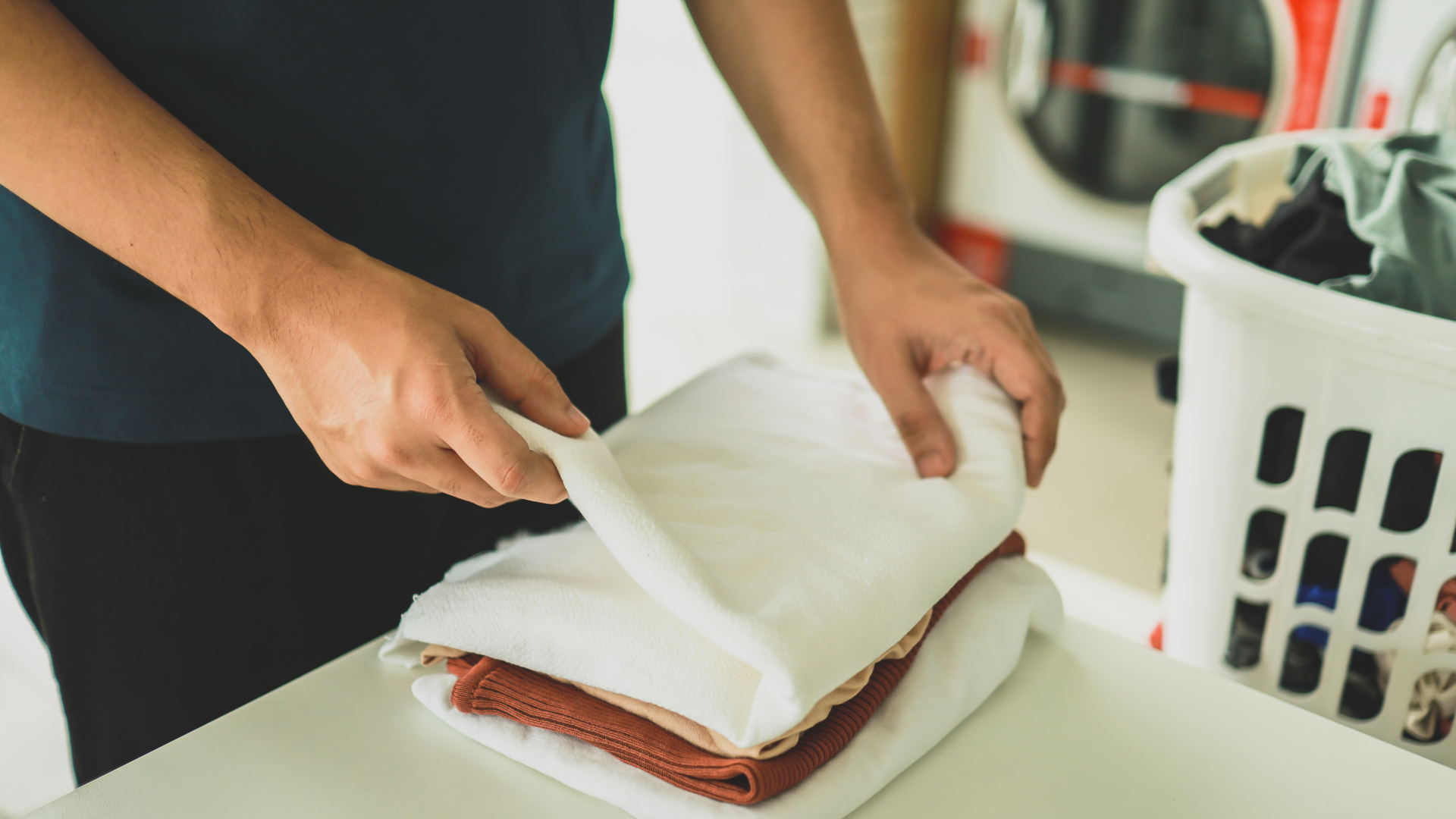 A man is folding towels on a table in a laundromat.