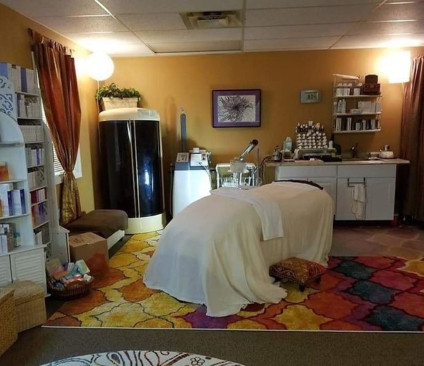 Spa room with massage table, sauna, and shelves of products; colorful rug.