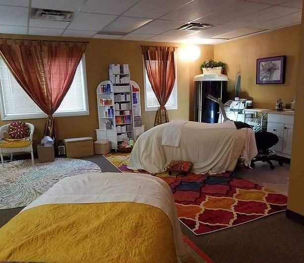 Massage therapy room with two beds, warm colors, and product shelves.