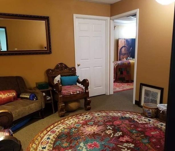 A room with a patterned rug, ornate chair, couch, mirror, and door to another room.