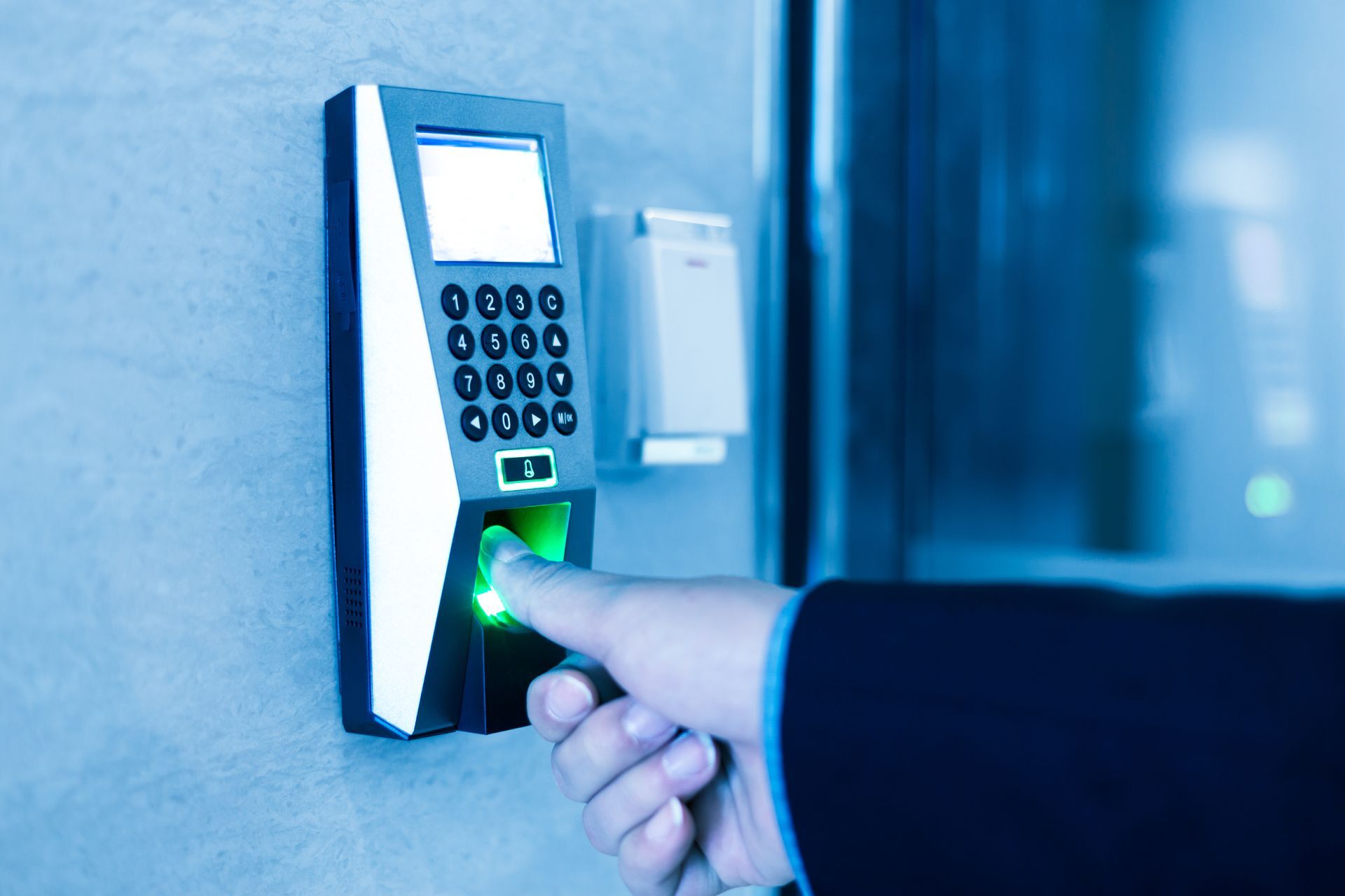 A biometric fingerprint scanner with a numeric keypad mounted on a wall.