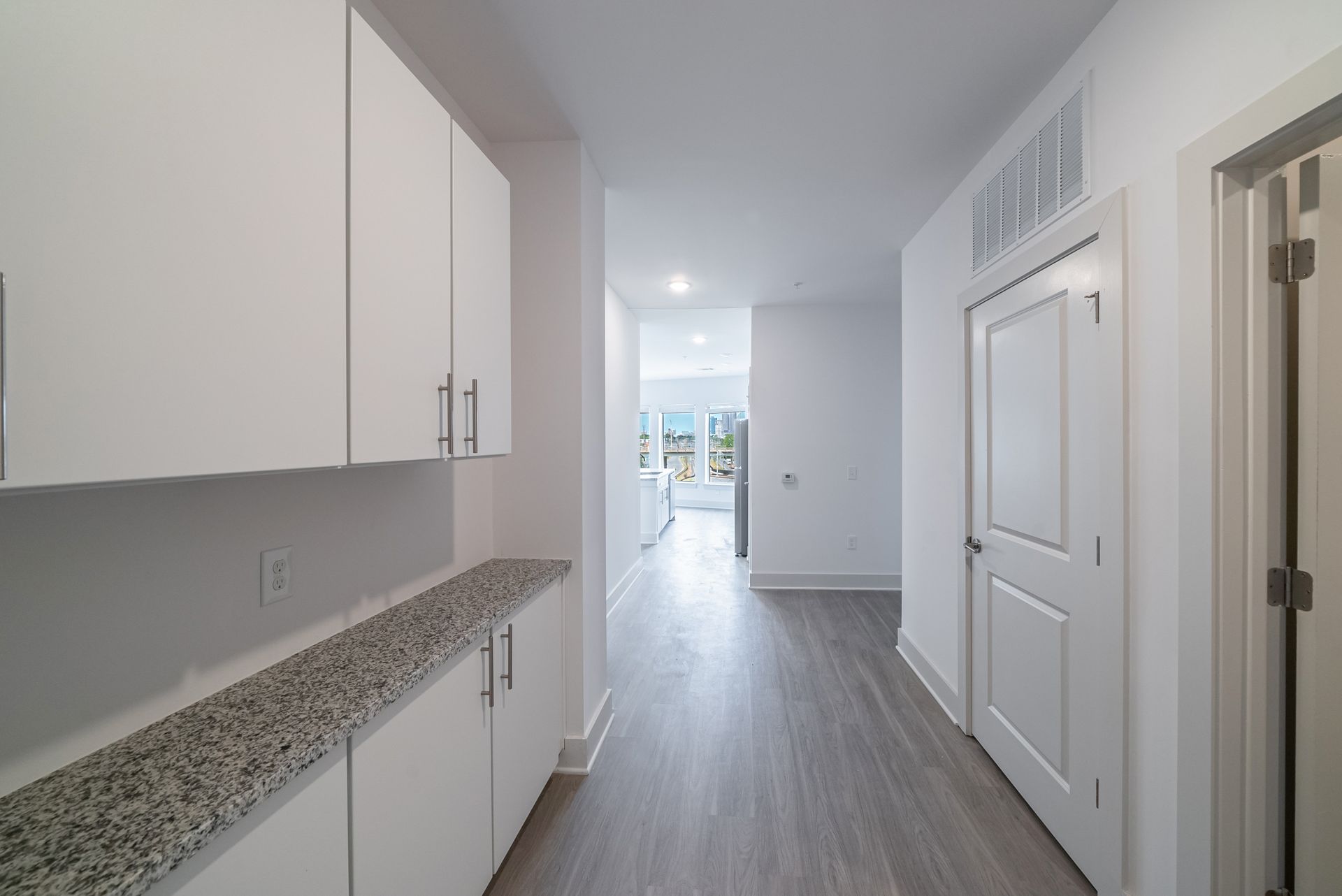 Narrow hallway with white cabinets, granite countertop, and a door.