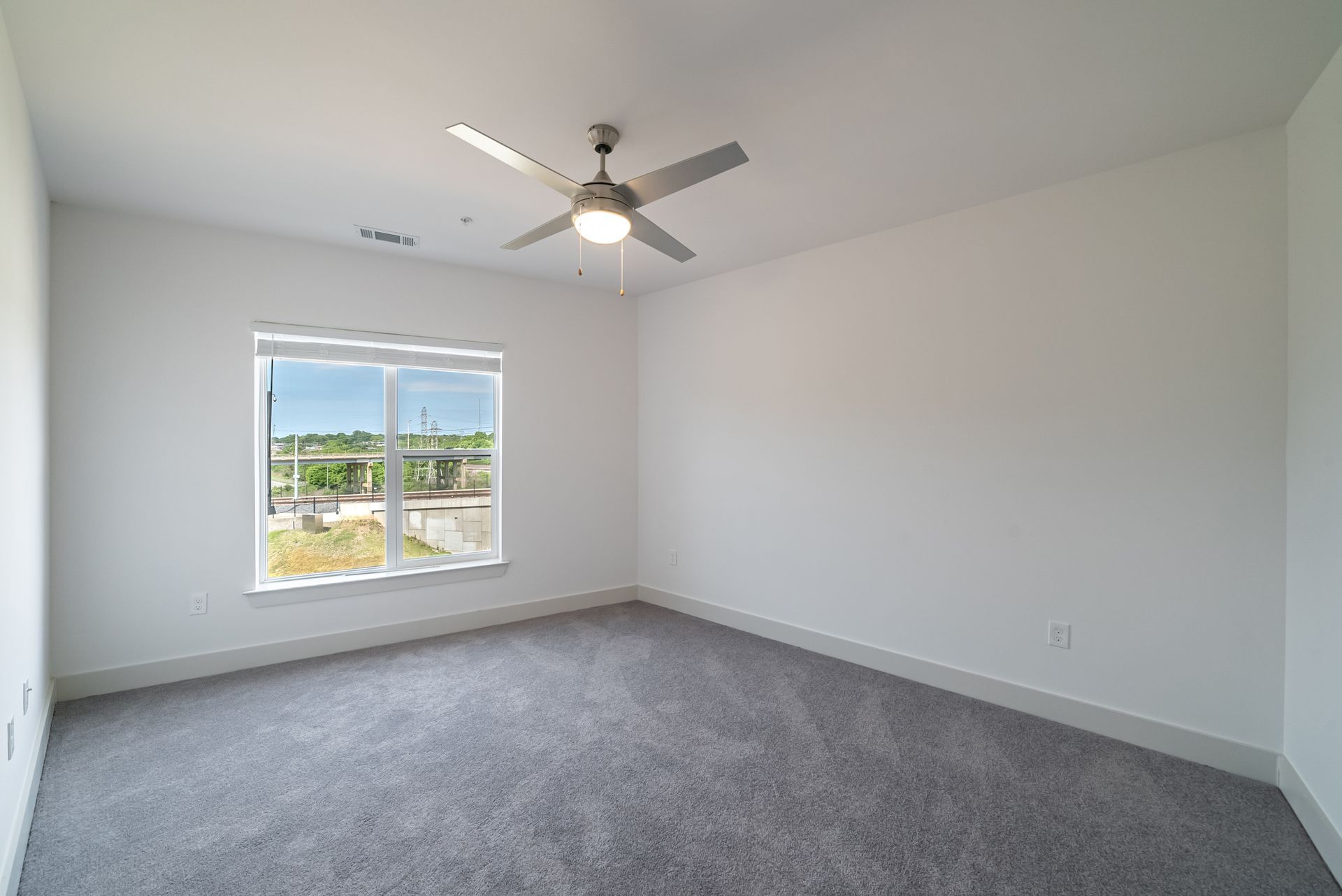 Empty bedroom with grey carpet, a window, and a ceiling fan.