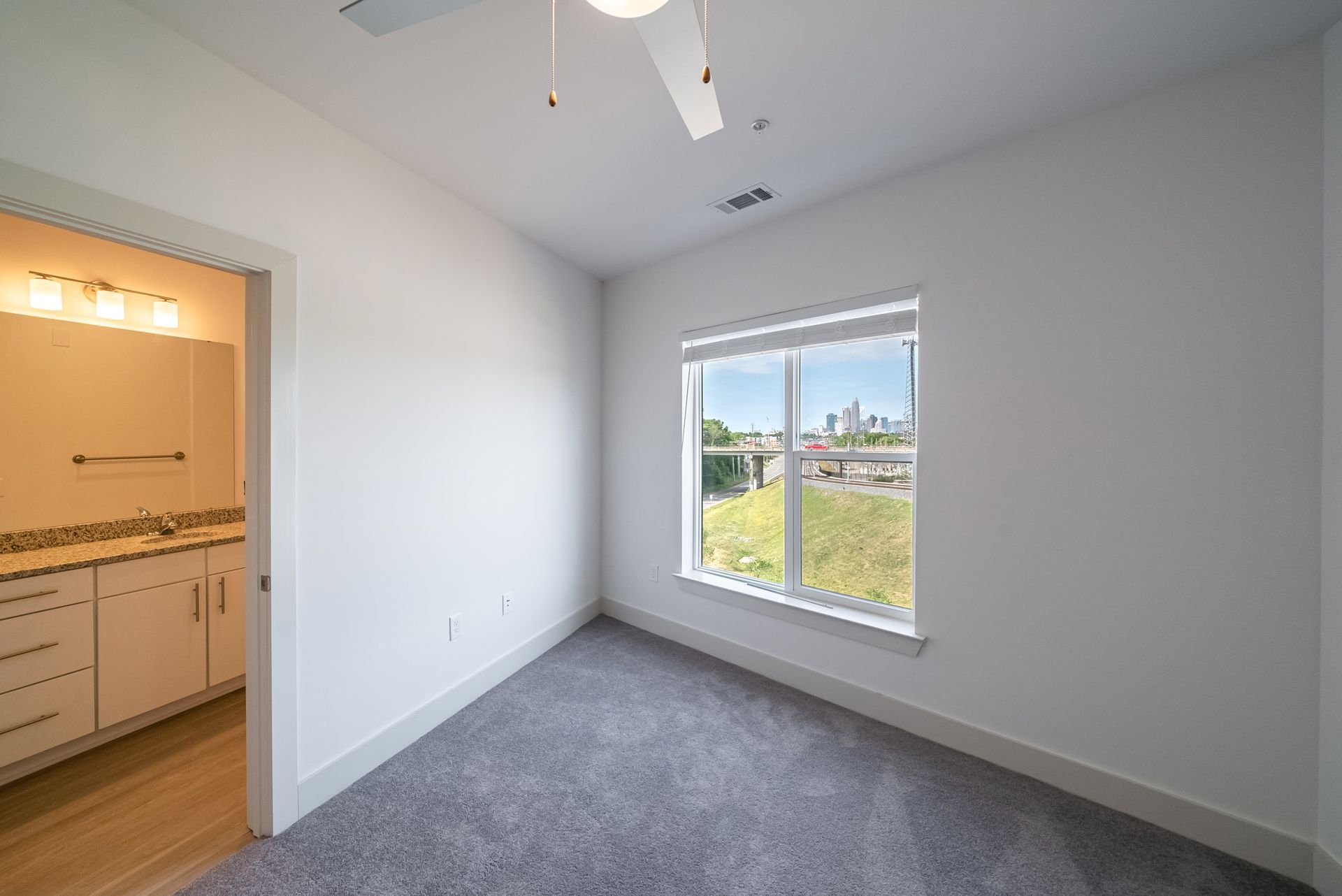 Empty bedroom with a window and an open doorway to a bathroom with a vanity.