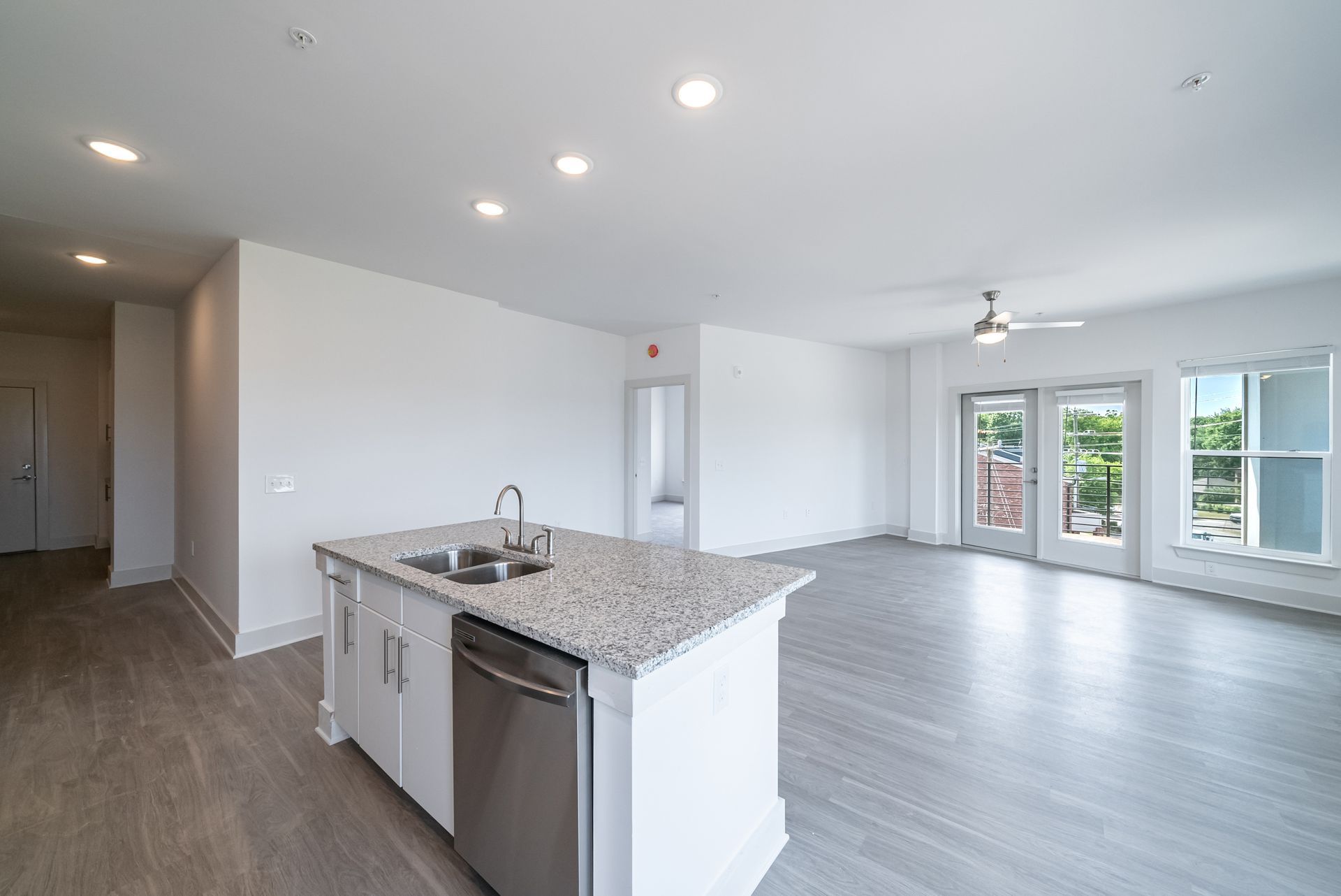Open-concept kitchen with a granite countertop island, stainless steel appliances, and a view of a balcony and windows.