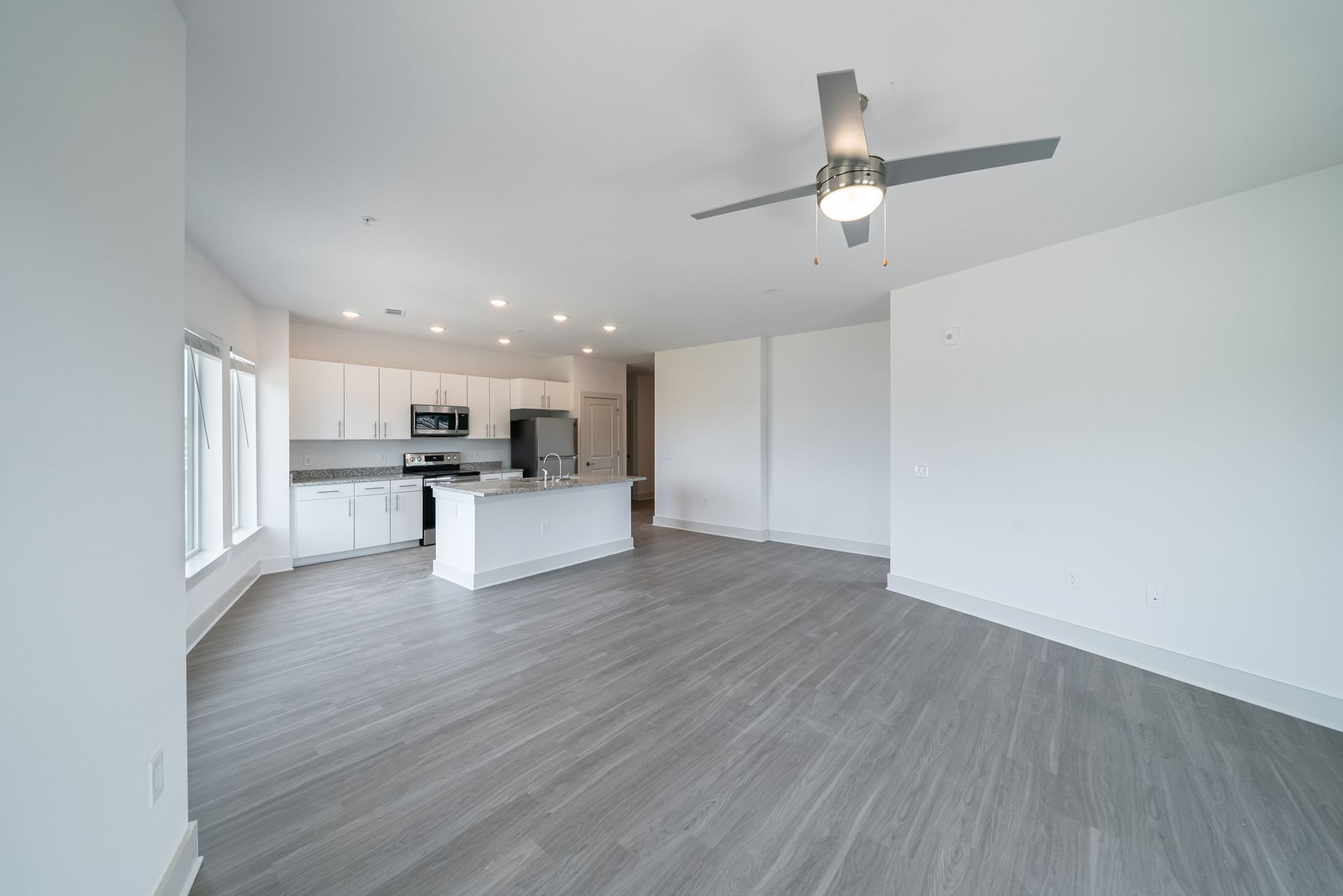 Open-concept kitchen and living area with gray flooring, white cabinets, and a ceiling fan.