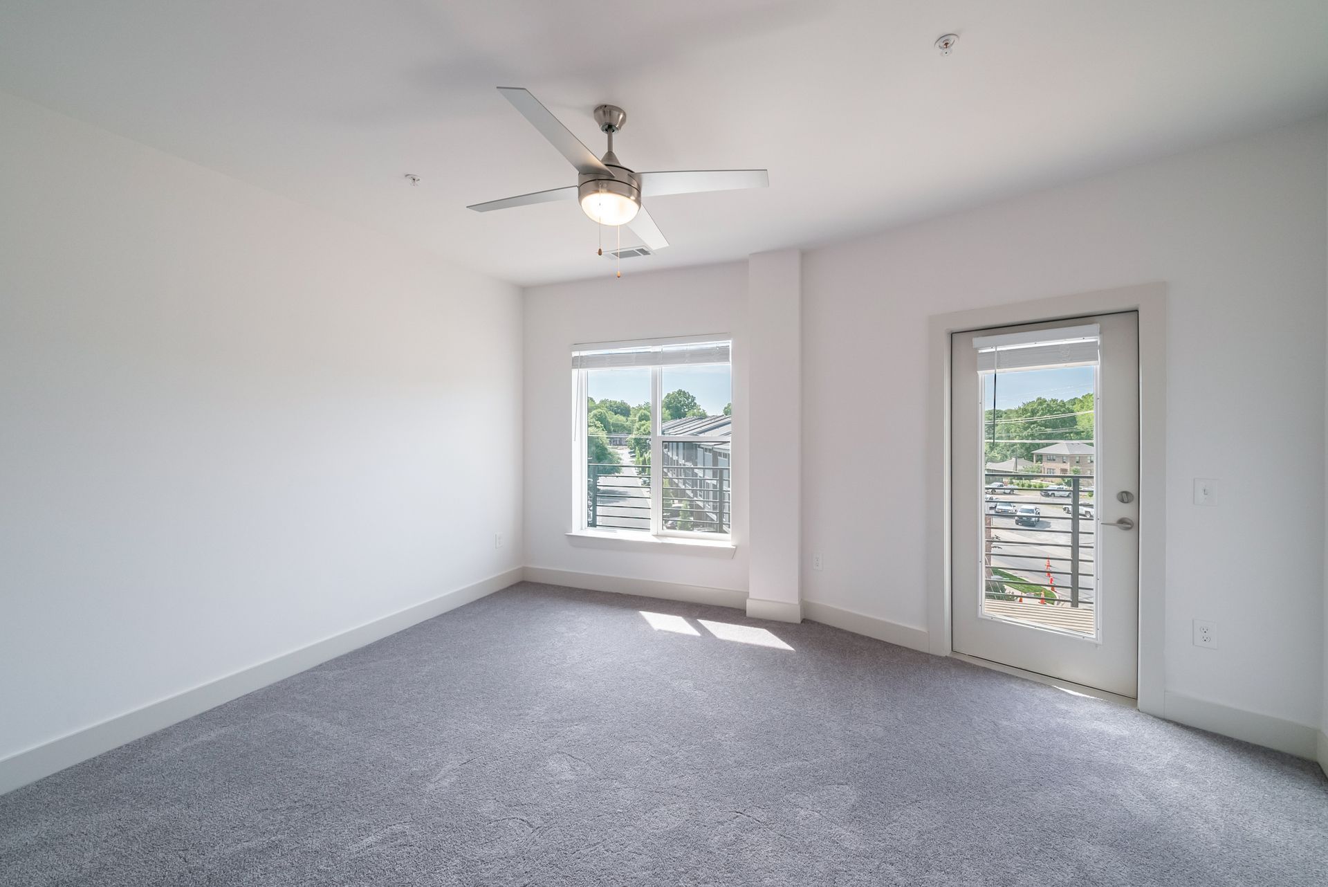 Empty room with gray carpet, white walls, a window, and a door to a balcony.
