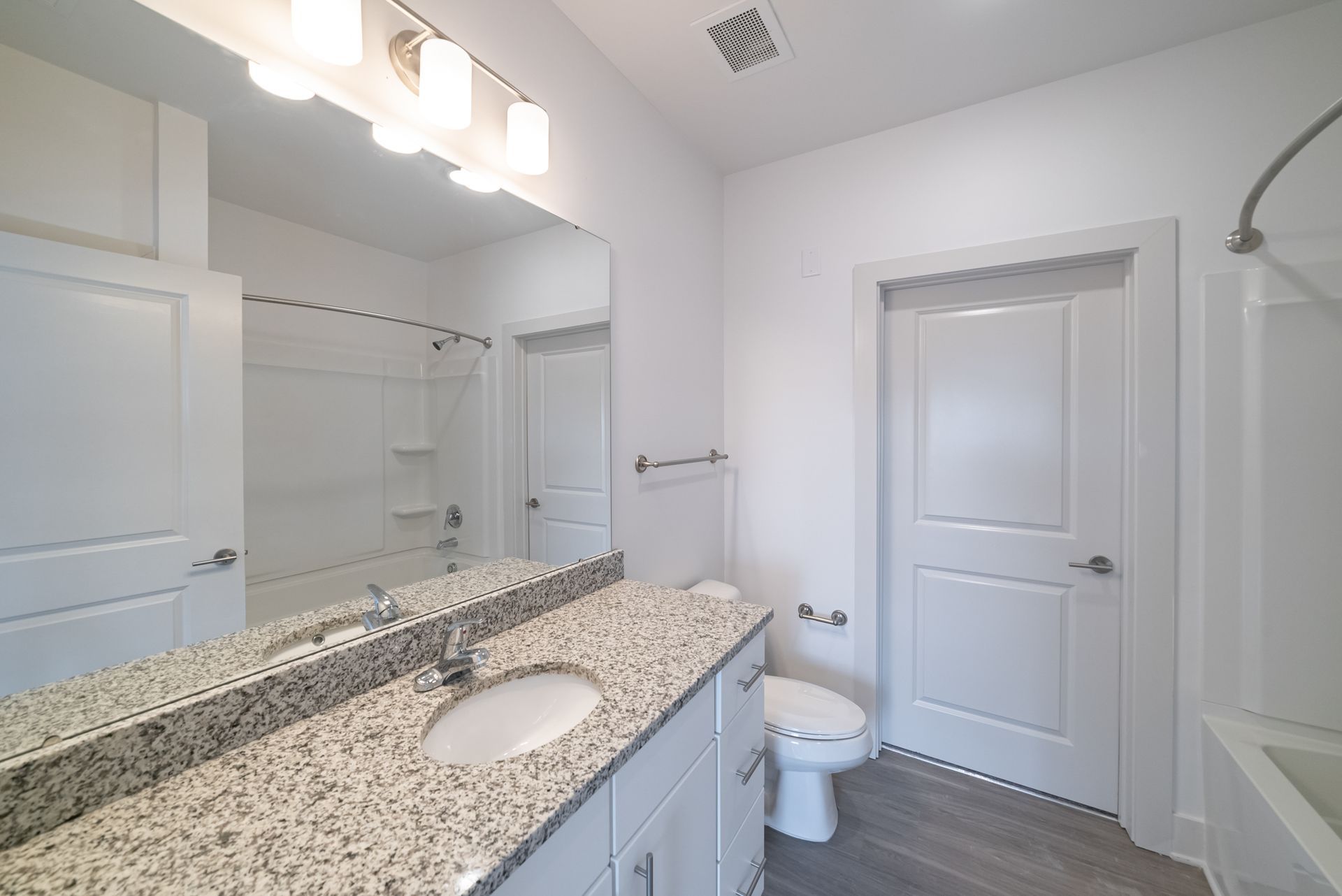 Bathroom with white walls, granite countertop, and gray wood floor.