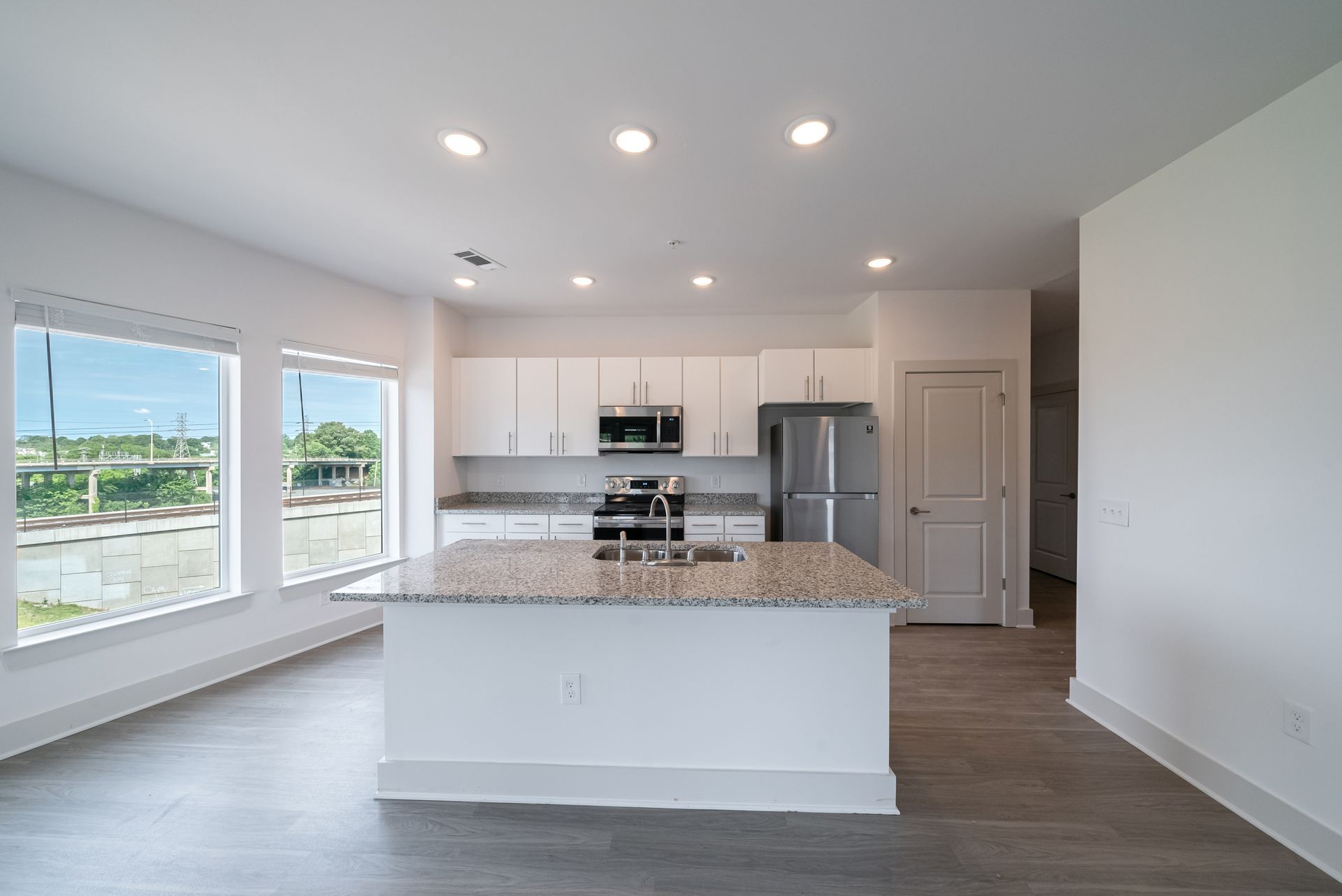 Modern kitchen with white cabinets, granite island, stainless steel appliances, and large windows.