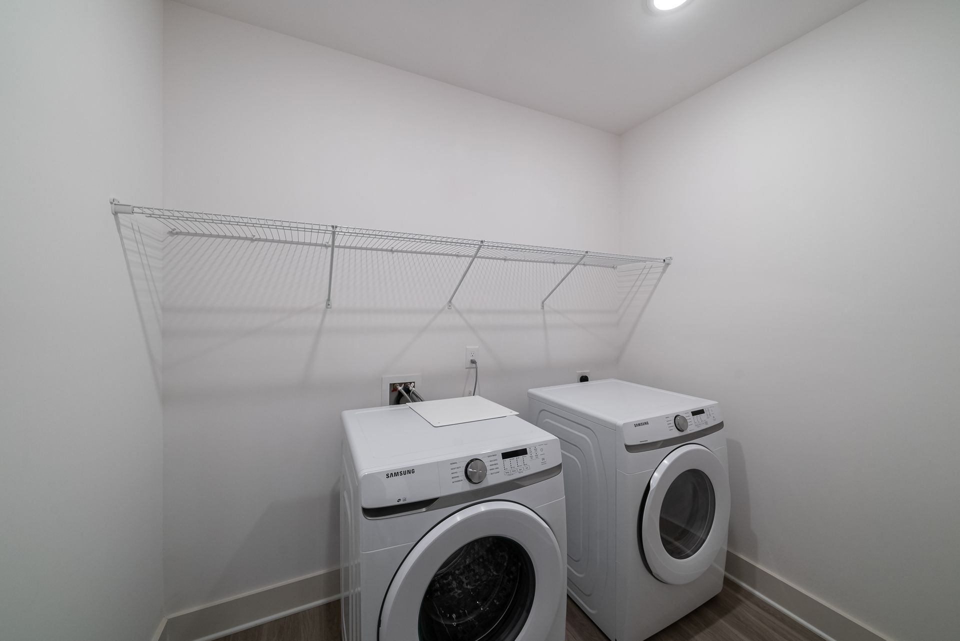 Laundry room with white washer and dryer, wire shelf, and light-colored walls.