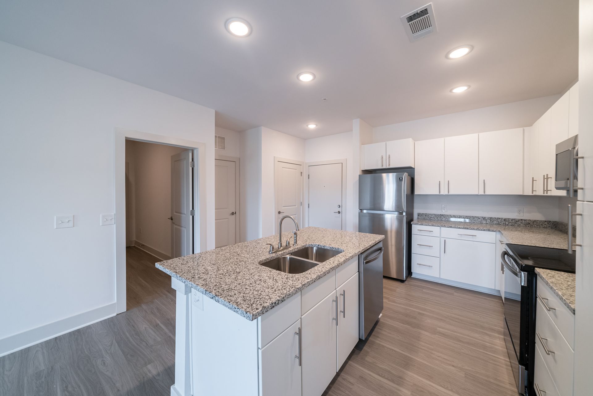 Modern white kitchen with island, stainless steel appliances, granite countertops, and light wood floors.