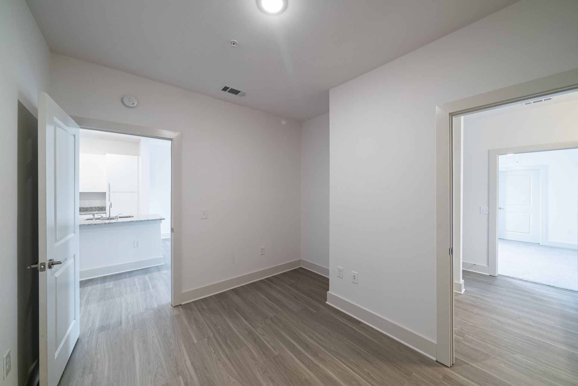 Empty apartment hallway with wood floors and white walls.