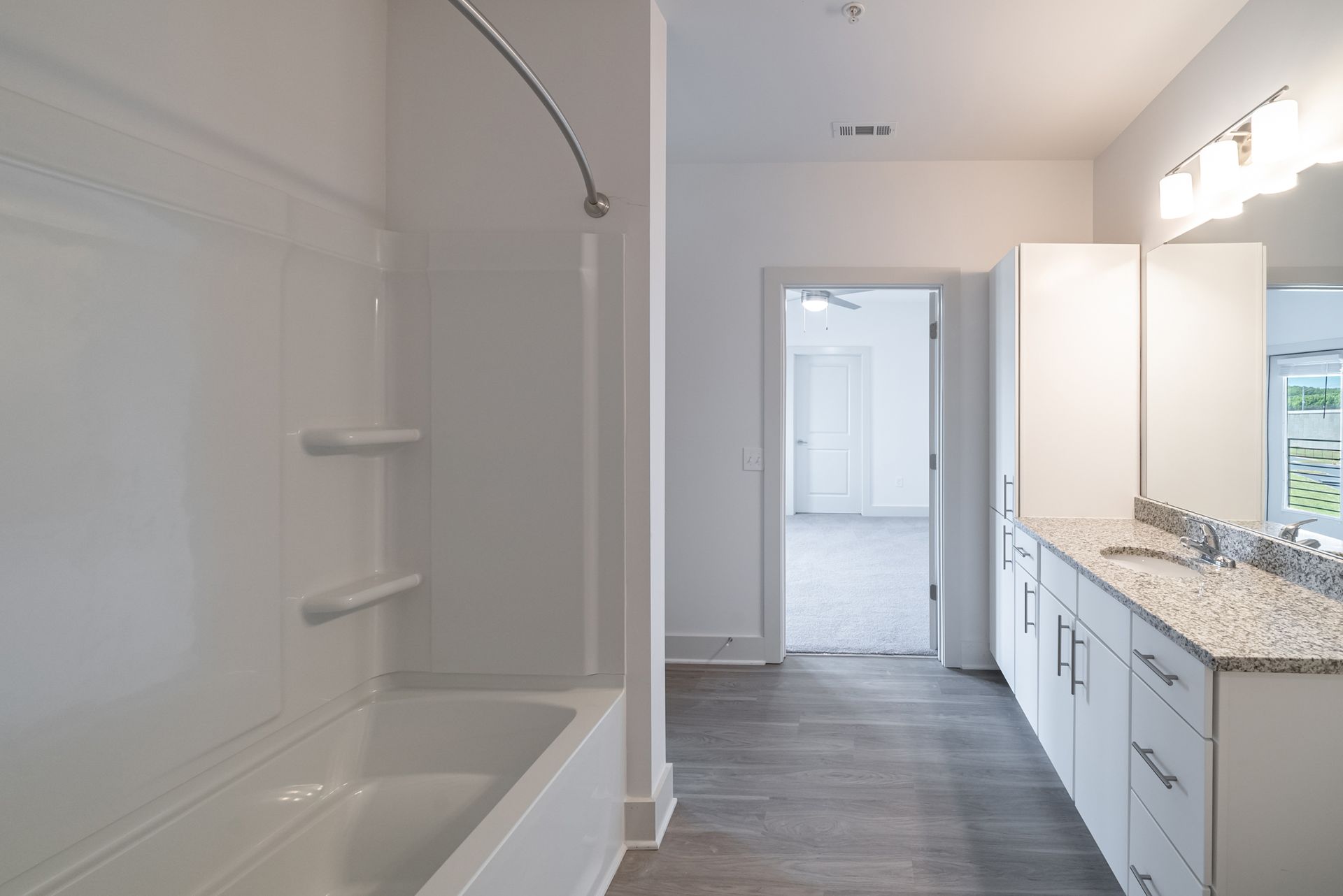 White bathroom with a shower, vanity, and open door to a room with light flooring.