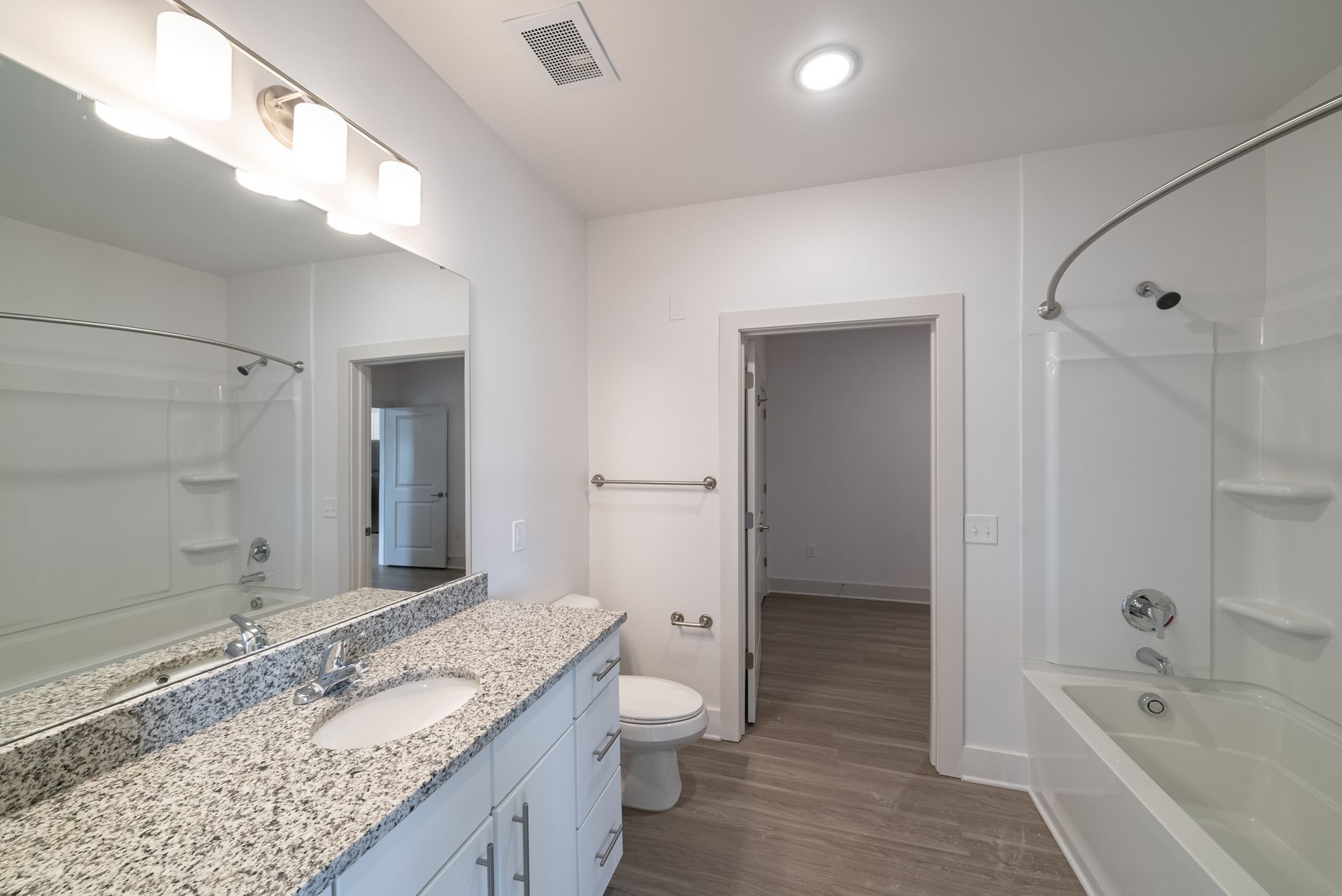 Bright bathroom with granite countertop, white fixtures, and a doorway to another room.