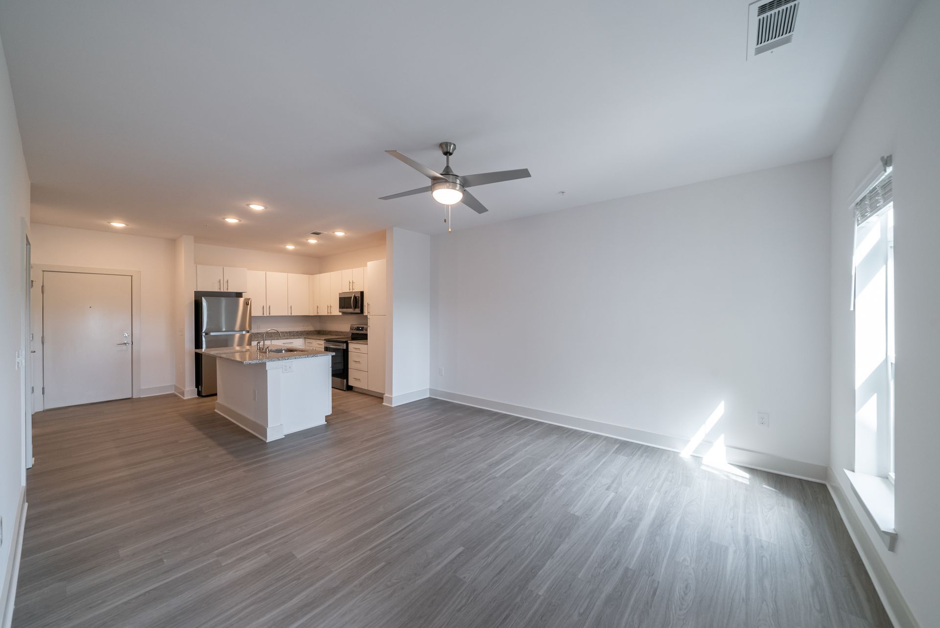 Open-concept apartment: Kitchen island, stainless steel appliances, gray wood flooring, and large windows.