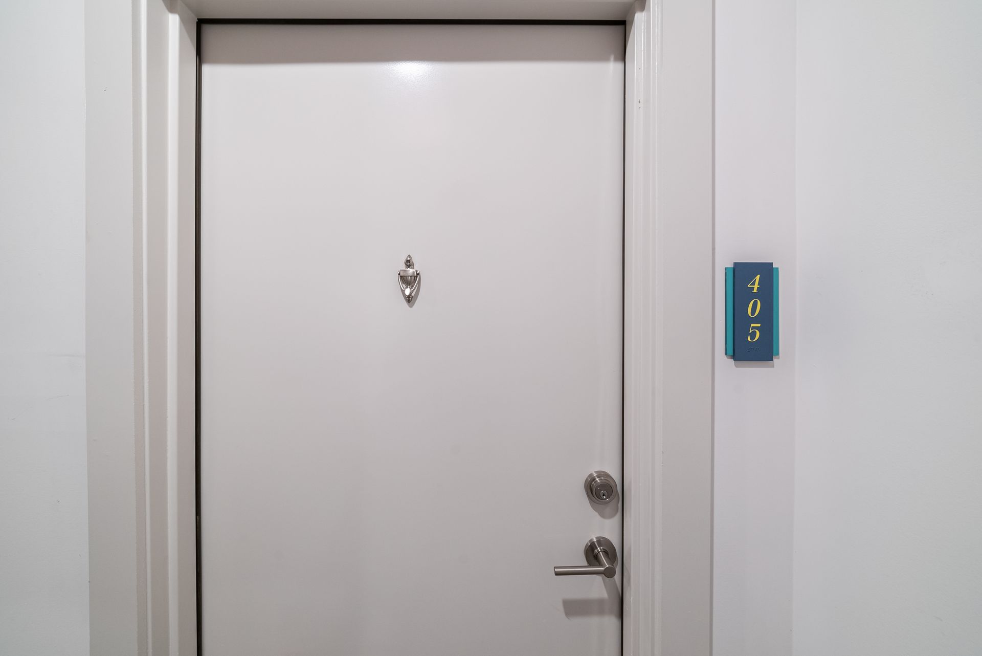 White door with a knocker and doorknob, next to a wall with a blue room number 105.