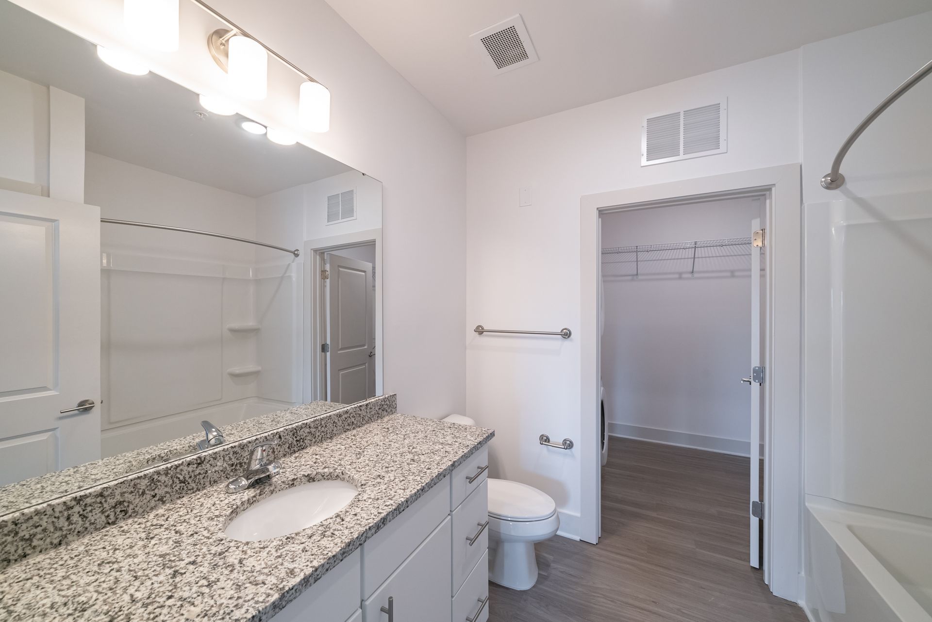 White bathroom with granite countertop, toilet, shower, and walk-in closet.