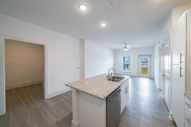 Modern apartment kitchen and living area with white walls and island.