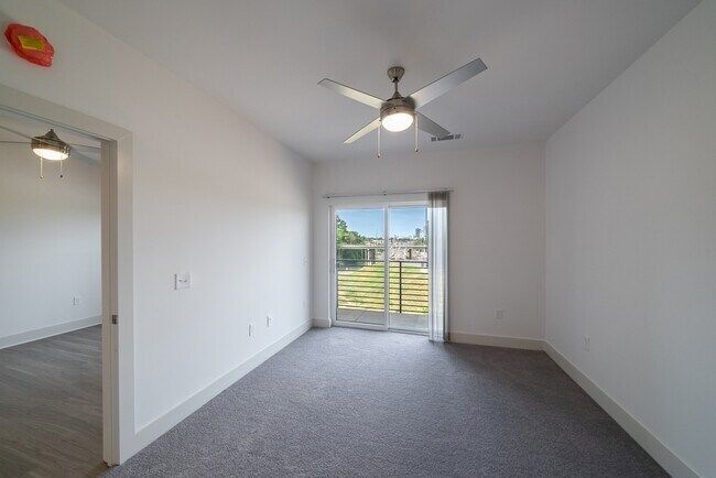Empty bedroom with gray carpet, white walls, sliding glass door, and ceiling fan.