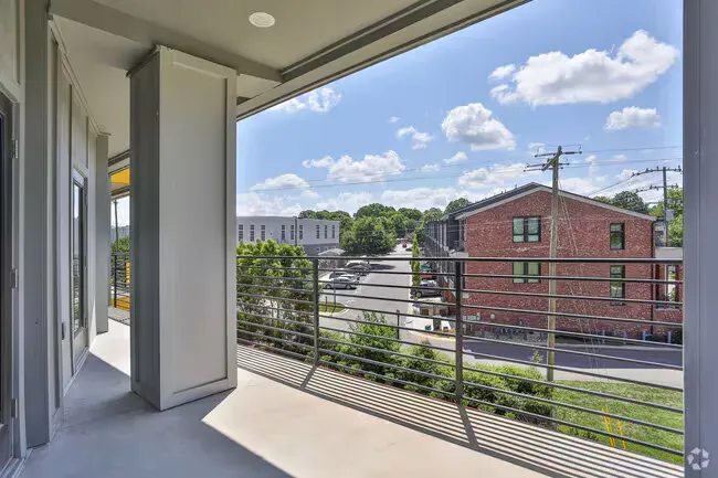 Balcony view: metal railing, gray concrete, buildings, trees, and a blue sky with clouds.