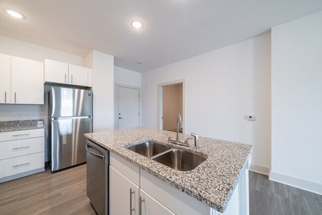 Modern kitchen with white cabinets, stainless steel appliances, gray granite island with sink, and light wood flooring.