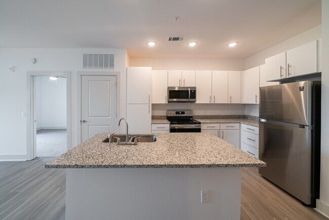 Modern white kitchen with island, granite countertops, and stainless steel appliances.