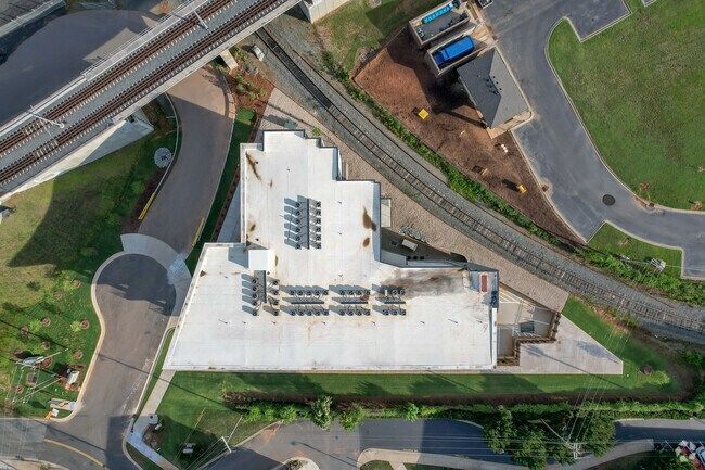Aerial view of a building with a white roof, next to train tracks and a road, with some green landscaping.