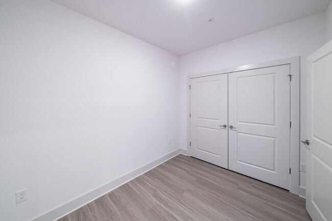 Empty white room with wood-look flooring and white closet doors.