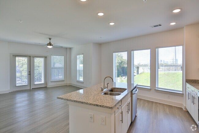 Bright kitchen with white cabinets, granite countertop, stainless steel appliances, and large windows overlooking green grass.