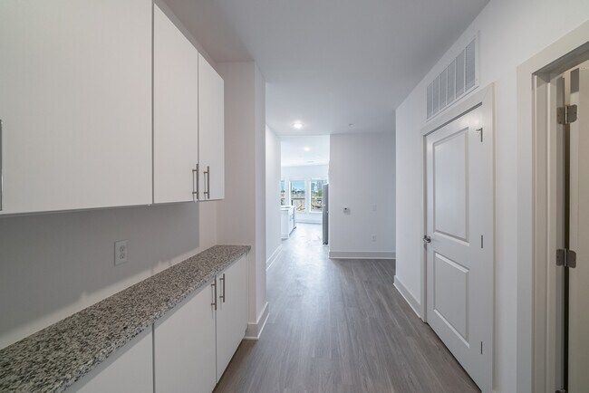 Long hallway with white cabinets and door, gray flooring, and light at the end.