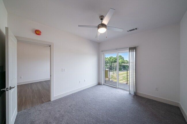 Empty bedroom with gray carpet, white walls, and a sliding glass door to a balcony.