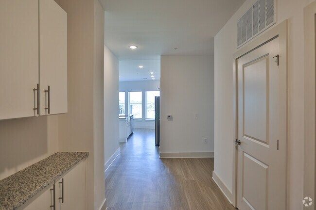 Narrow hallway with white cabinets, light wood floors, and a door.