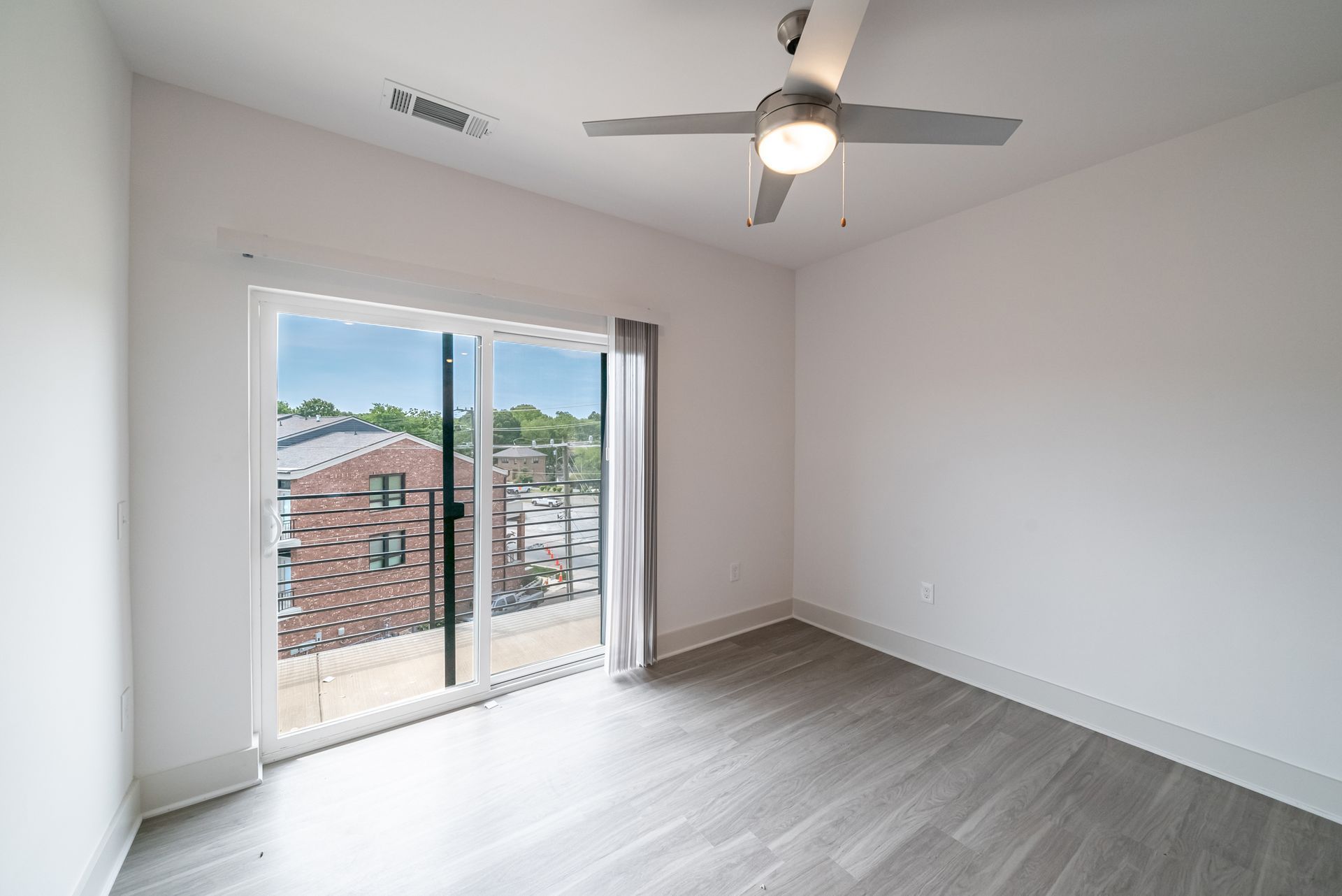 Empty bedroom with sliding glass doors to a balcony, grey flooring, and a ceiling fan.