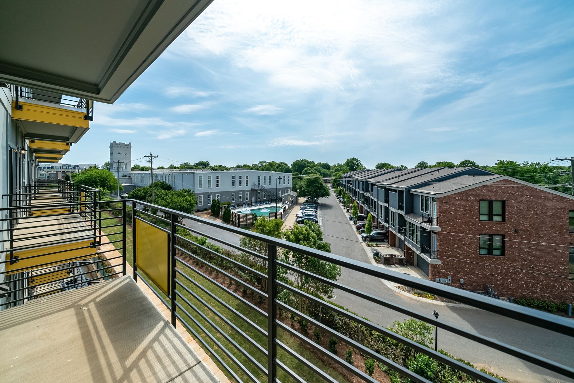 View from a balcony overlooking a street with townhouses and blue sky.