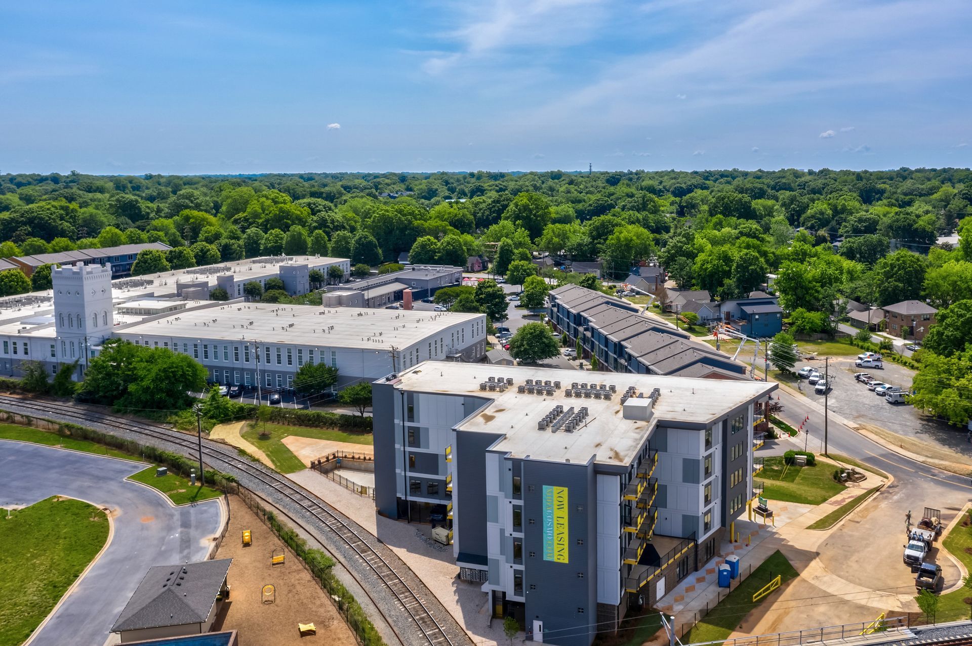 Aerial view of modern apartment buildings and surrounding lush green trees under a blue sky.