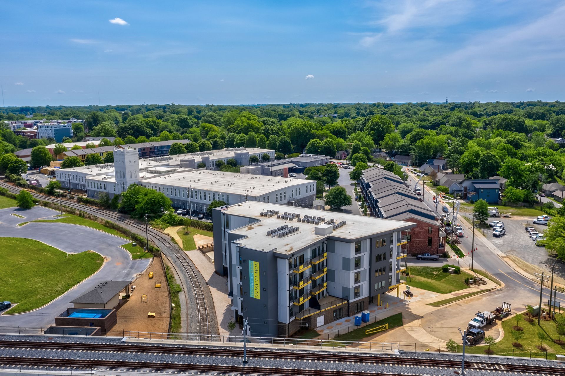 Aerial view of modern apartment buildings, a railway, and trees on a sunny day.