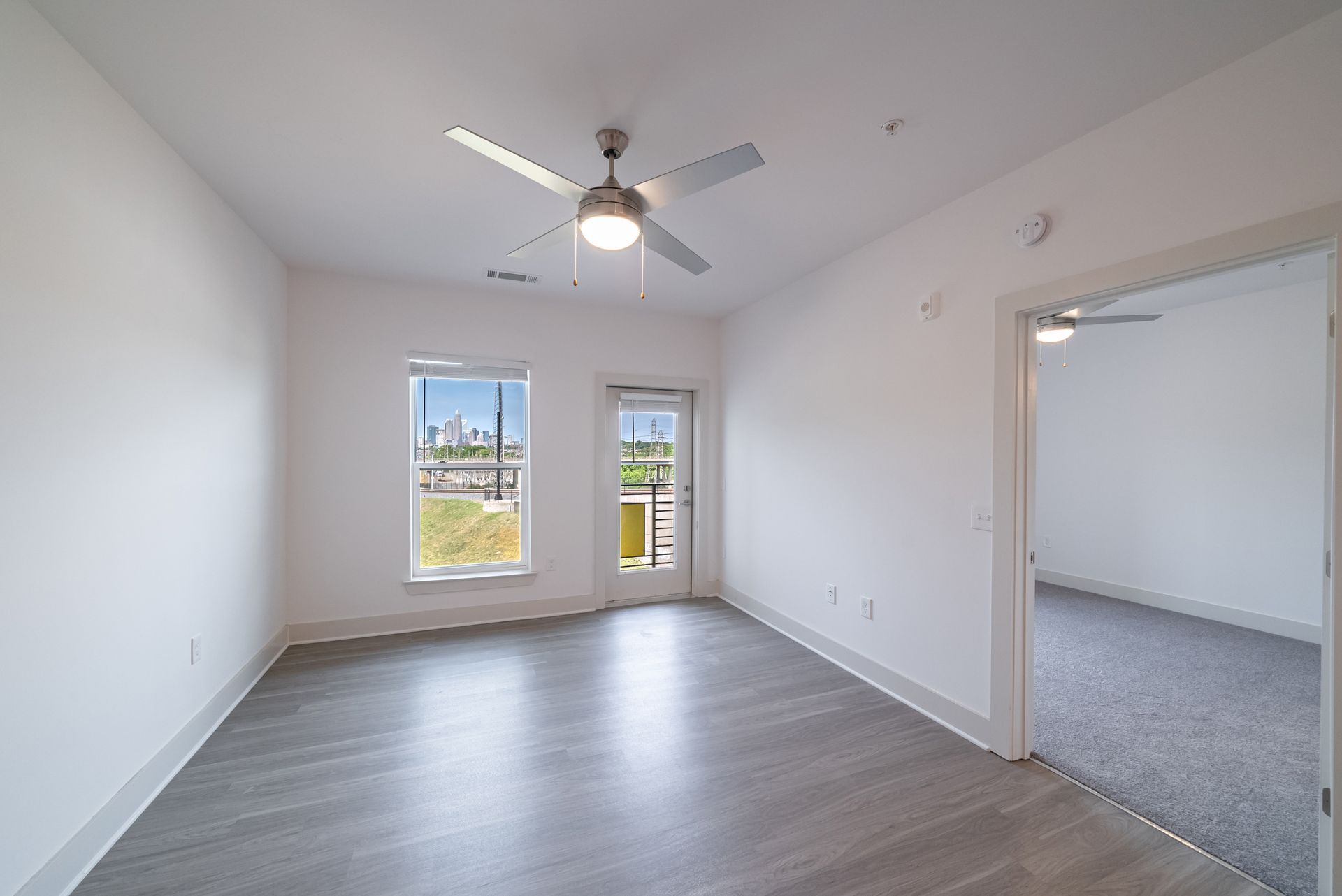 Empty room with gray floors, white walls, windows, and a ceiling fan.