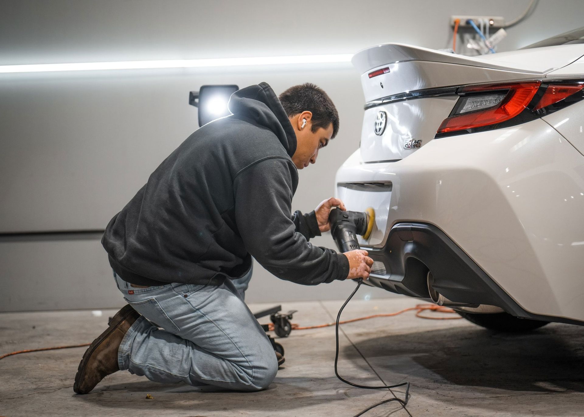A man is kneeling down and polishing the back of a white car.
