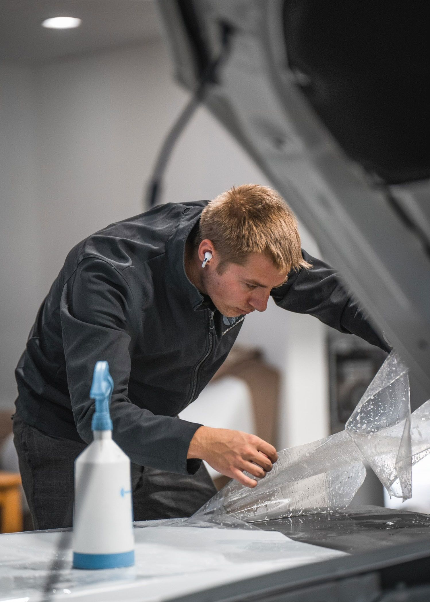 A man is applying a protective film to the hood of a car.