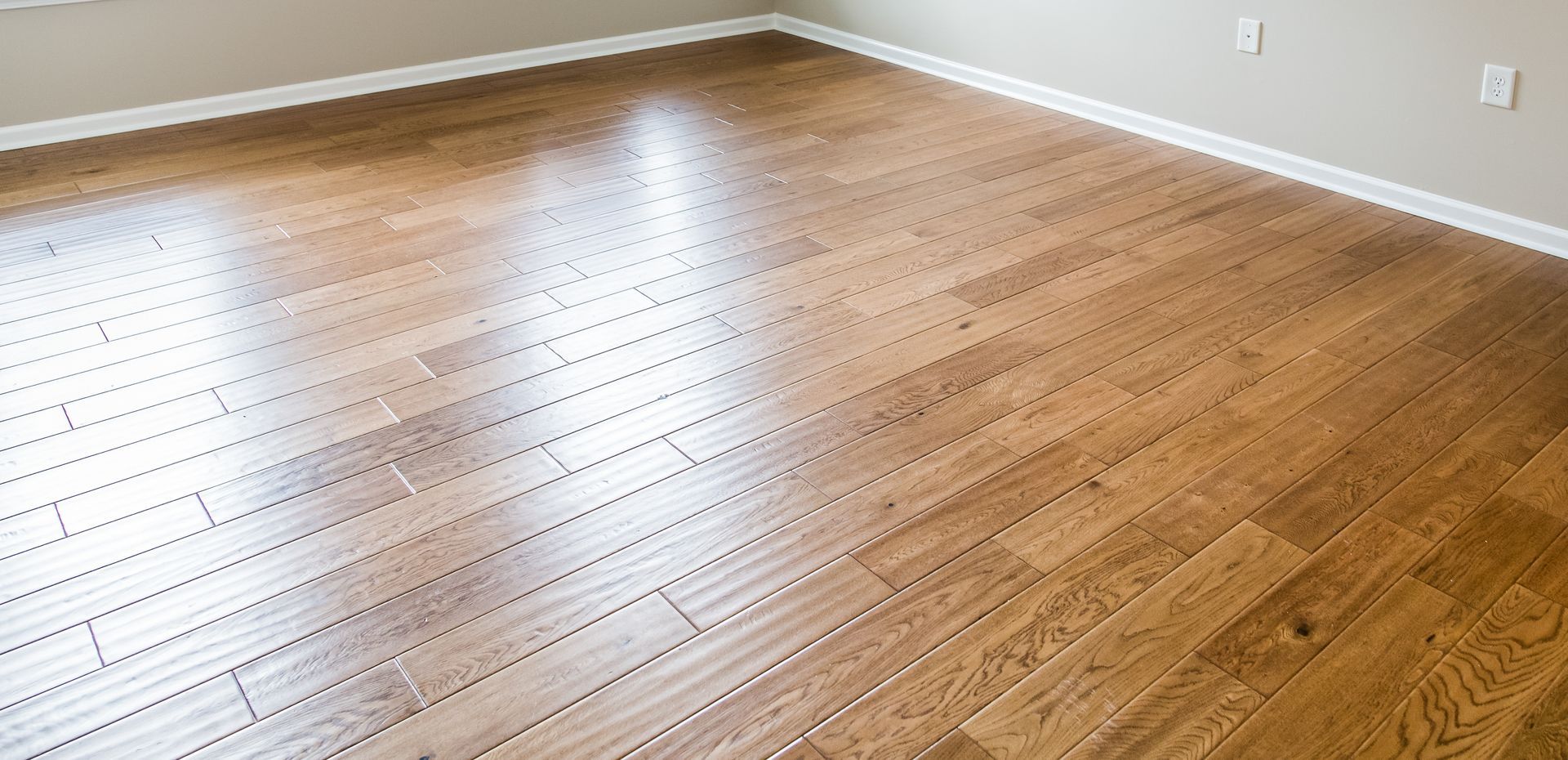 A wooden floor in an empty room with a white trim.