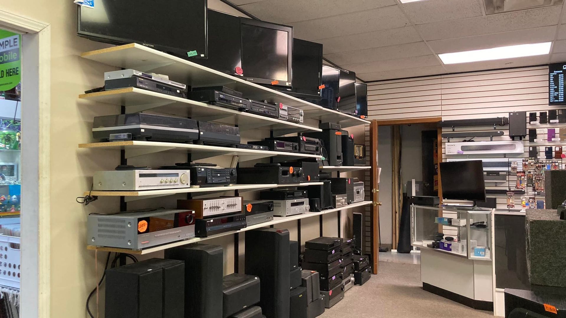 Shelves displaying electronics in a store. TVs, receivers, and speakers are visible.