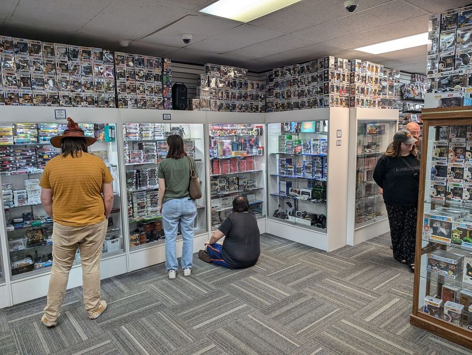People browse items in a store, many items in glass display cases, walls covered in photos.