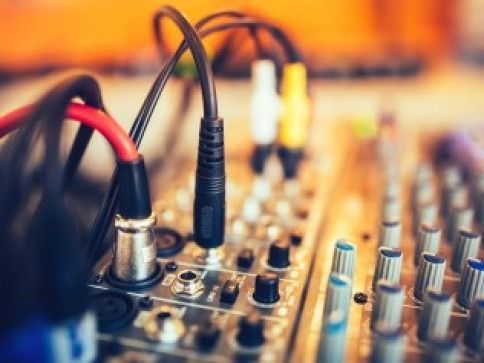 Audio mixer with connected cables, close-up, knobs and jacks visible, blurred background.