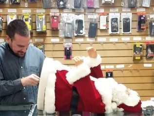 Man adjusting Santa Claus decoration in a store with phone accessories displayed on the wall.