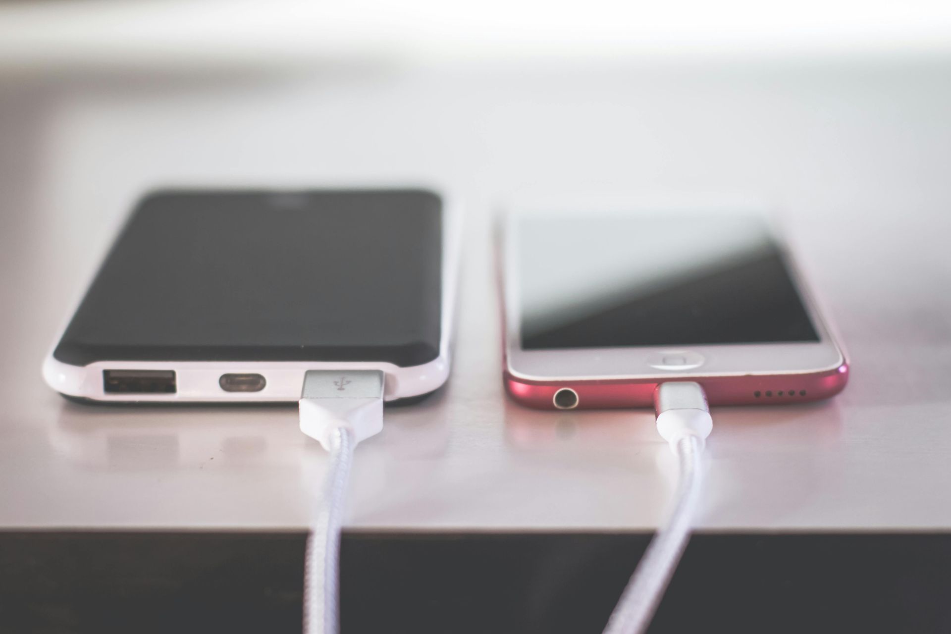 Two smartphones, one black and one red, charging with white USB cables.