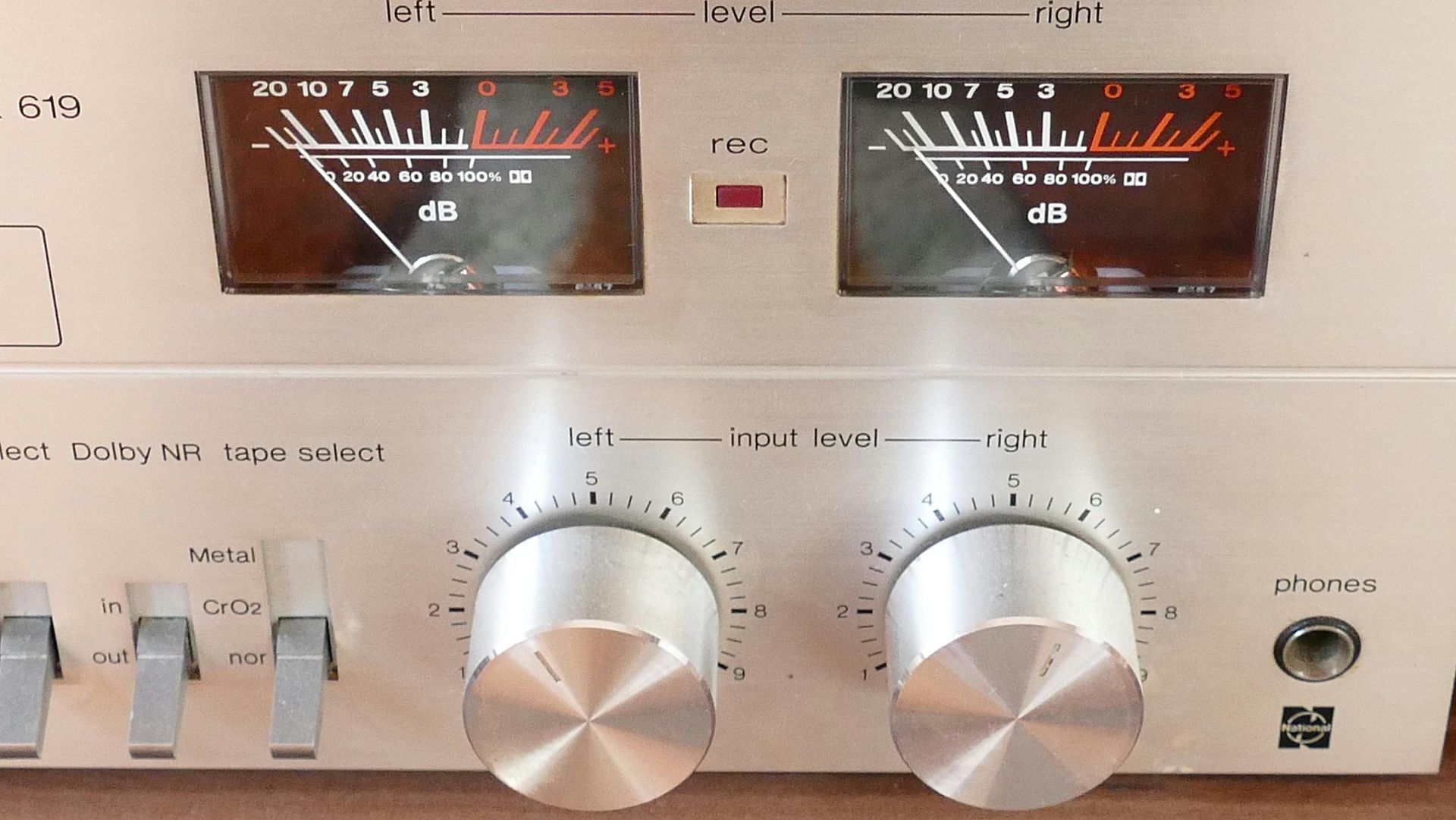 Close-up of a silver audio amplifier with two VU meters and control knobs. The meters show red and white levels.